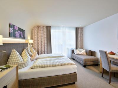 Jasny pokój hotelowy z dwoma pojedynczymi łóżkami, sofą, biurkiem i dużym oknem.