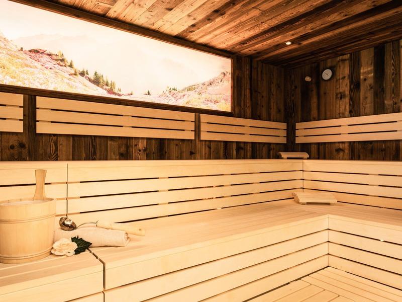 Jasna sauna z drewnianymi ławkami, obraz górski na ścianie i akcesoria do sauny.