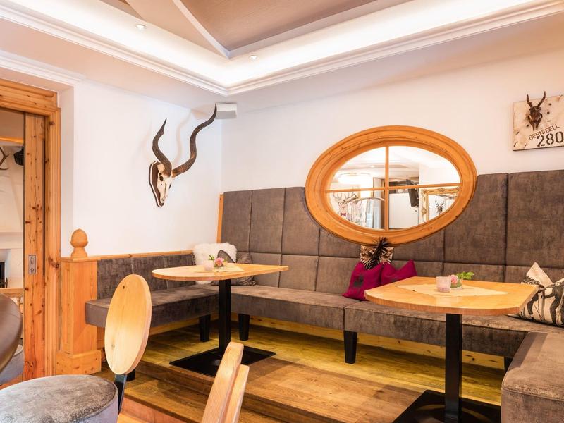 Przytulny salon z tapicerowanymi ławkami, drewnianymi meblami i ciepłym oświetleniem sufitowym.