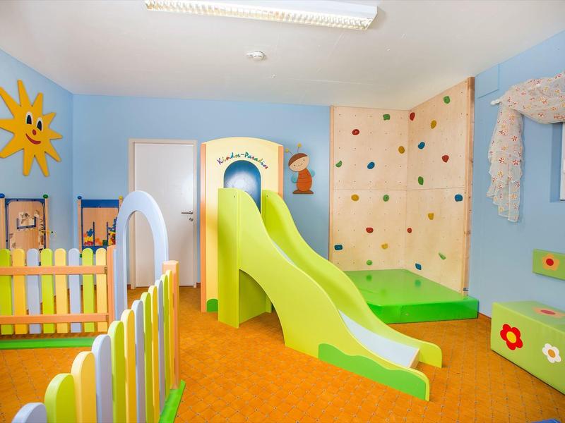 Kolorowy, kryty plac zabaw dla dzieci z zjeżdżalnią, ścianką wspinaczkową i miękką podłogą.