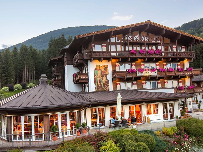 Tradycyjny hotel z kolorowymi skrzynkami na kwiaty i zadbanym ogrodem w górskiej scenerii.