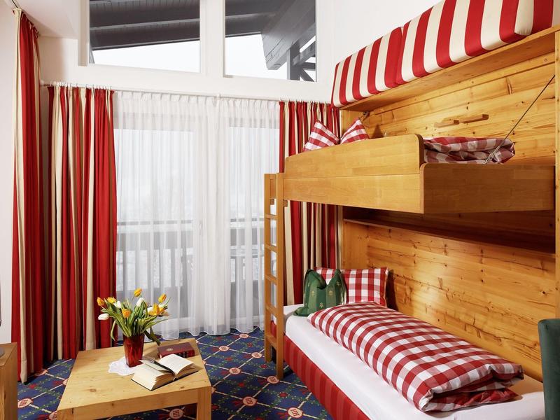 Przytulny pokój hotelowy z łóżkiem piętrowym, czerwoną i białą kratowaną pościelą oraz oknem z zasłonami