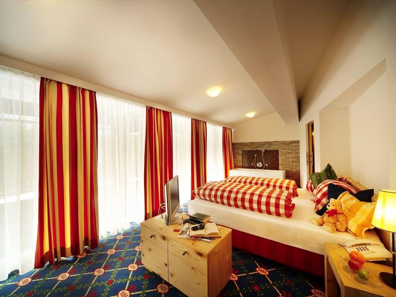 Jasny pokój hotelowy z dużym łóżkiem, pasiastymi zasłonami i przytulnym oświetleniem.