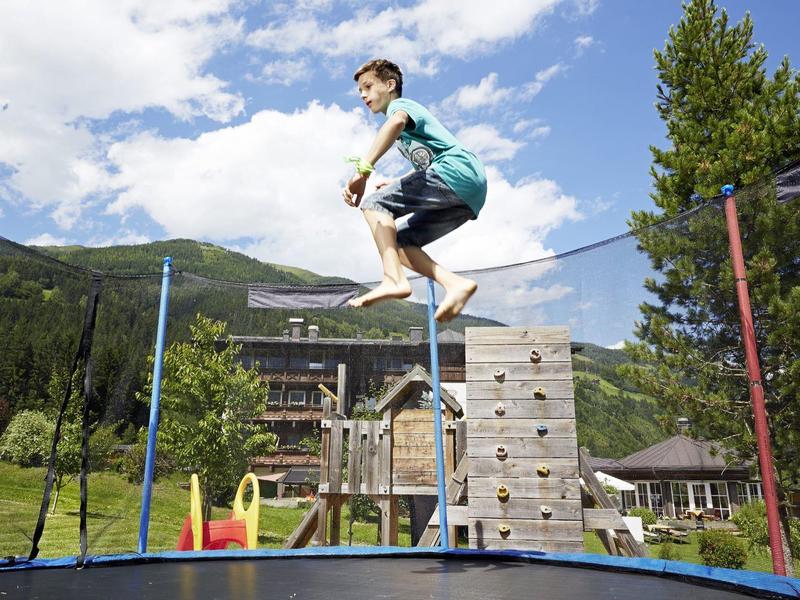 Chłopiec skacze na trampolinie na tle górskiego krajobrazu i placu zabaw.