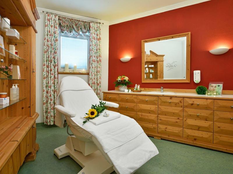 Pokój relaksacyjny z wygodnym fotelem, drewnianymi meblami i ciepło oświetlonym lustrem.