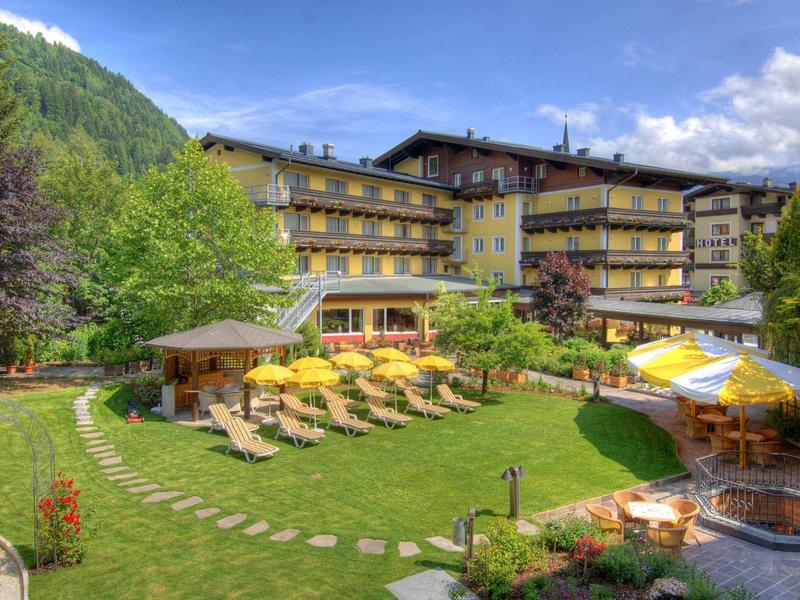 Hotel s lehátky a slunečníky na zeleném trávníku před alpskou scenérií.