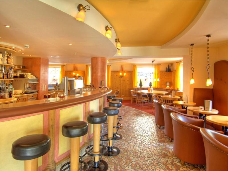 Pohodlný hotelový bar s pultem, barovými židlemi a posezením s koženými křesly a stoly.
