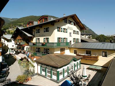 Mehrstöckiges weißes Haus mit grün-weißen Fensterläden in sonniger Berglandschaft.