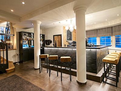 Gemütliche Bar mit Holzboden, dunkelgrauer Theke, Stühlen und weiß getönten Säulen.