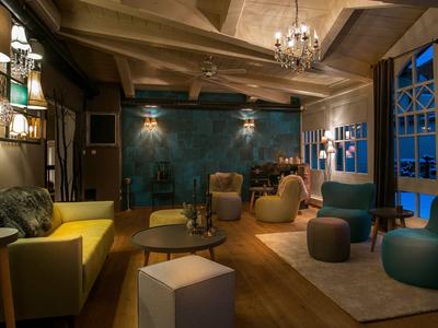 Pohodlná hotelová lounge se světlým osvětlením, křesly, pohovkami a dekorativními dřevěnými prvky.