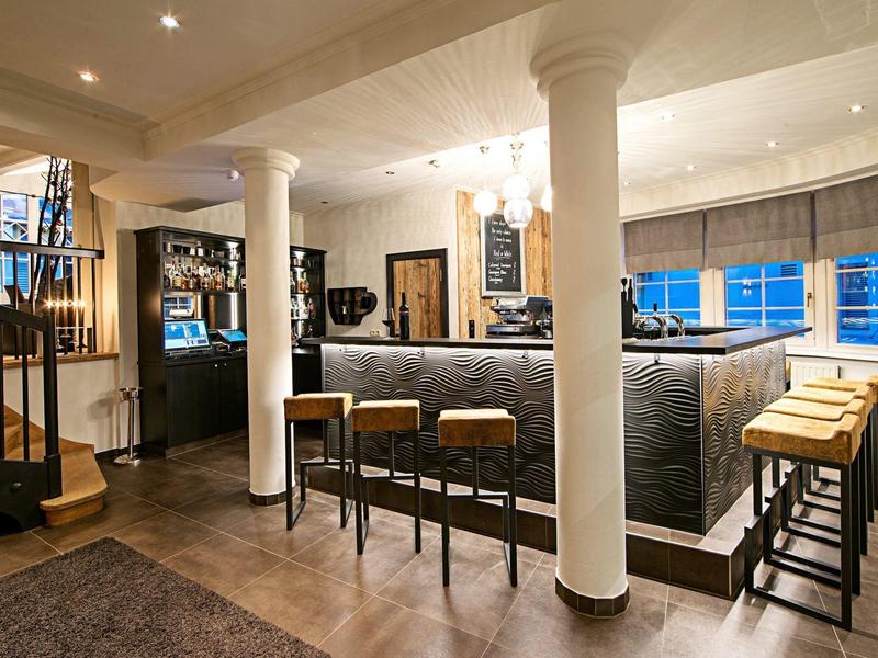 Gemütliche Bar mit Holzboden, dunkelgrauer Theke, Stühlen und weiß getönten Säulen.