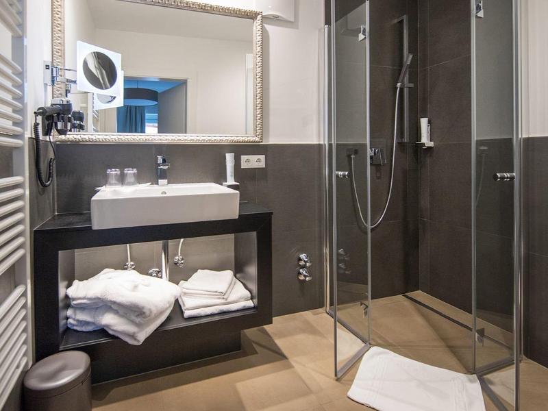 Moderne Dusche mit Glasabtrennung, Untertischwaschbecken, großem Spiegel und Handtüchern in hellem Bad.