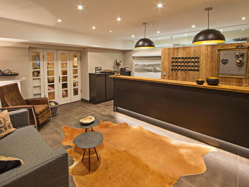 Moderner Empfangsbereich mit Holztheke, Ledersesseln, Teppich und warmen Lichtquellen.