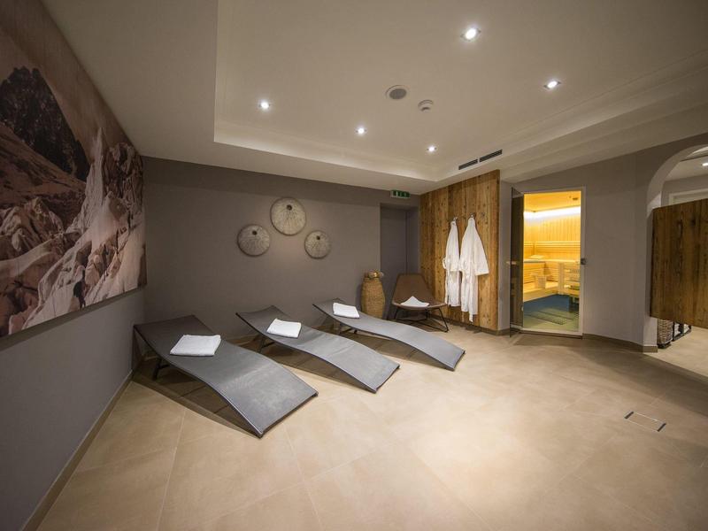 Ruheraum mit drei grauen Liegen, runden Wanddekorationen und offenem Zugang zu Saunabereich.