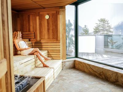 Žena odpočívá v sauně s velkými okny s výhledem na zasněžené stromy.