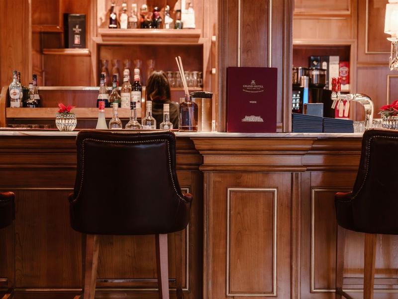 Elegantní hotelový bar s tmavými barovými židlemi a dobře zásobenými regály v pozadí.