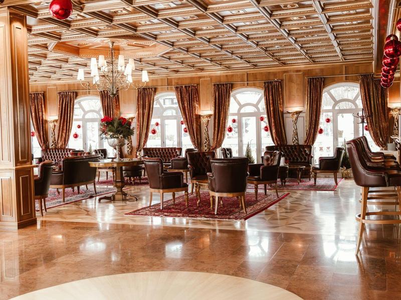 Elegantní hotelová lounge se dřevěným obložením, křesly a lustry.