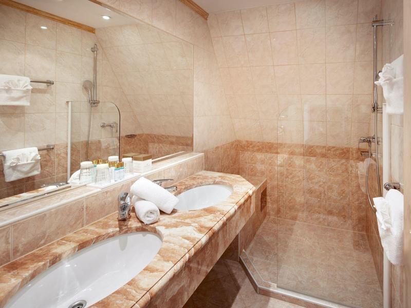 Moderní koupelna se skleněným sprchovým koutem, umyvadlem a hnědo-béžovými dlaždicemi