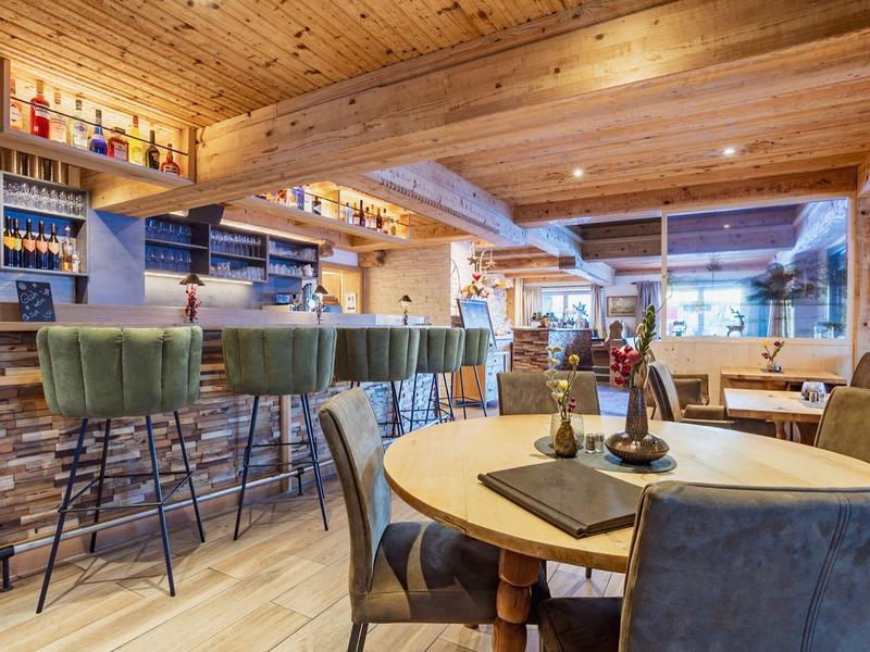 Acogedor bar de hotel con techo de madera, taburetes y mesas bajo luz cálida.