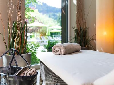 Gemütlicher Massagetisch mit beigem Handtuch, Korb und Blick auf grüne Pflanzen und Berge draußen.