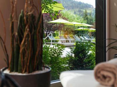Blick durch Fenster auf grüne Pflanzen, gelbe Sonnenschirme und Berge im Hintergrund.
