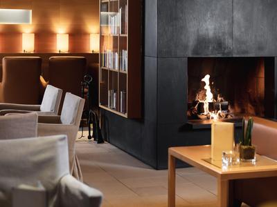 Salon d'hôtel confortable avec cheminée, tables et chaises sous une lumière chaleureuse.