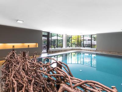 Moderner Innenpool mit rechteckiger Form, großen Fenstern und geschwungenem Holzkunstwerk davor.