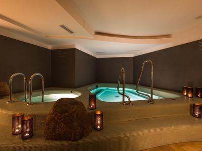 Innen-Spa mit zwei beleuchteten Whirlpools, warmem Licht und Kerzen auf glattem Boden.