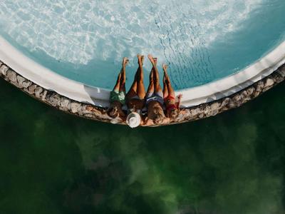 Trois personnes sont assises au bord d'une piscine ronde avec un environnement vert.