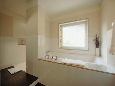 Helles Badezimmer mit Badewanne, Fenster, weißen Handtüchern und braunen Bodenfliesen.