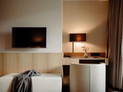 Modern eingerichtetes Zimmer mit Flachbildschirm, Schreibtisch, Lampe und weißen Sesseln.