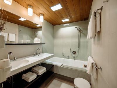 Modernes Bad mit Holzdecke, großer Spiegel, Doppelwaschbecken, Badewanne mit Duschvorhang, weißen Wänden.