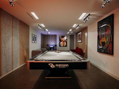 Ein heller, moderner Raum mit Billardtisch in der Mitte, Kunstwerken an den Wänden und Deckenleuchten.