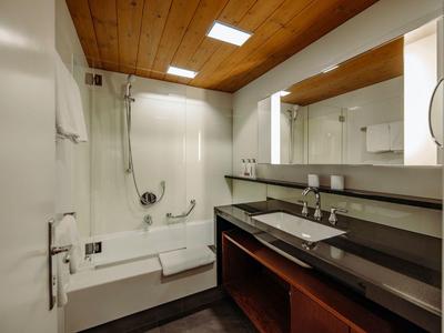 Modernes Badezimmer mit Holzdecke, großer Badewanne, langer Waschbeckenzeile und Spiegel.