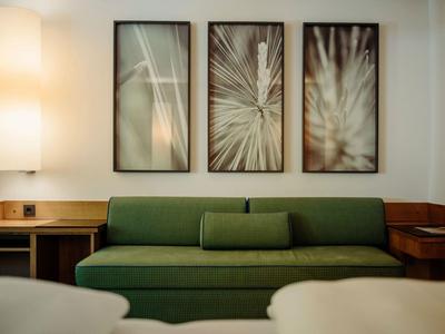 Modernes Wohnzimmer mit grünem Sofa, drei abstrakten Bildern und warmem Lampenlicht.