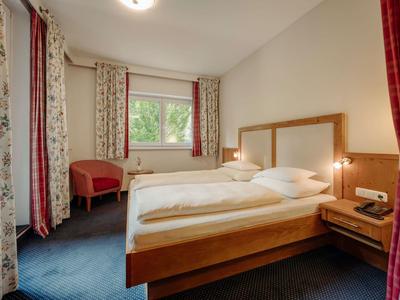 Gemütliches Schlafzimmer mit Doppelbett, Holzmöbeln, blauen Teppichboden und Vorhängen an Fenstern.