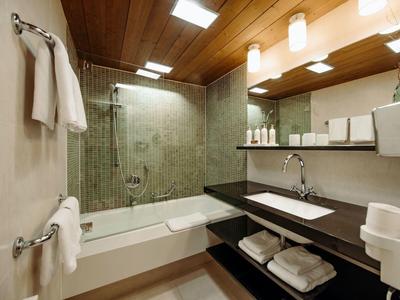 Modernes Bad mit Holzdecke, Wanne mit Glasduschwand, grüne Fliesen und großem Spiegel.