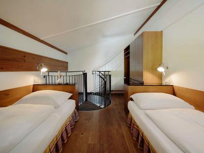 Zweibettzimmer mit Dachschräge, Holzvertäfelung und einer Wendeltreppe in der Mitte.