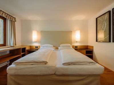 Schlichtes Hotelzimmer mit zwei Einzelbetten, Nachttischen und warmem Licht.