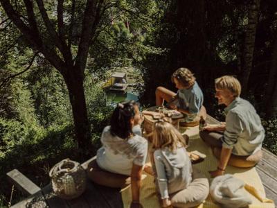 Quatre personnes assises détendues à une table en bois en plein air entourées d'arbres.
