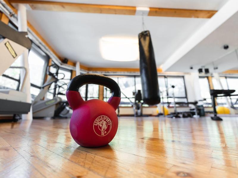 Ein rot-schwarzes Kettlebell-Gewicht liegt auf einem Holzfußboden in einem hellen Fitnessstudio.