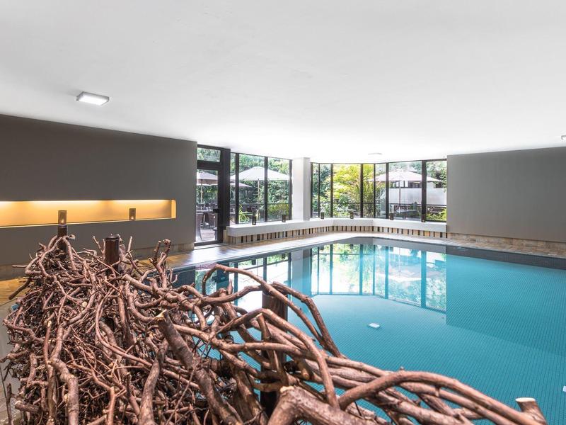 Moderner Innenpool mit rechteckiger Form, großen Fenstern und geschwungenem Holzkunstwerk davor.