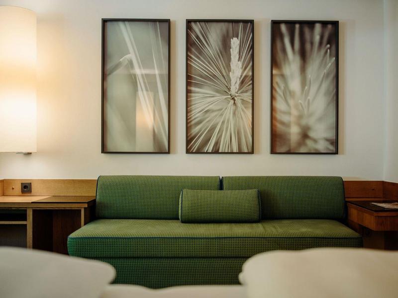 Modernes Wohnzimmer mit grünem Sofa, drei abstrakten Bildern und warmem Lampenlicht.