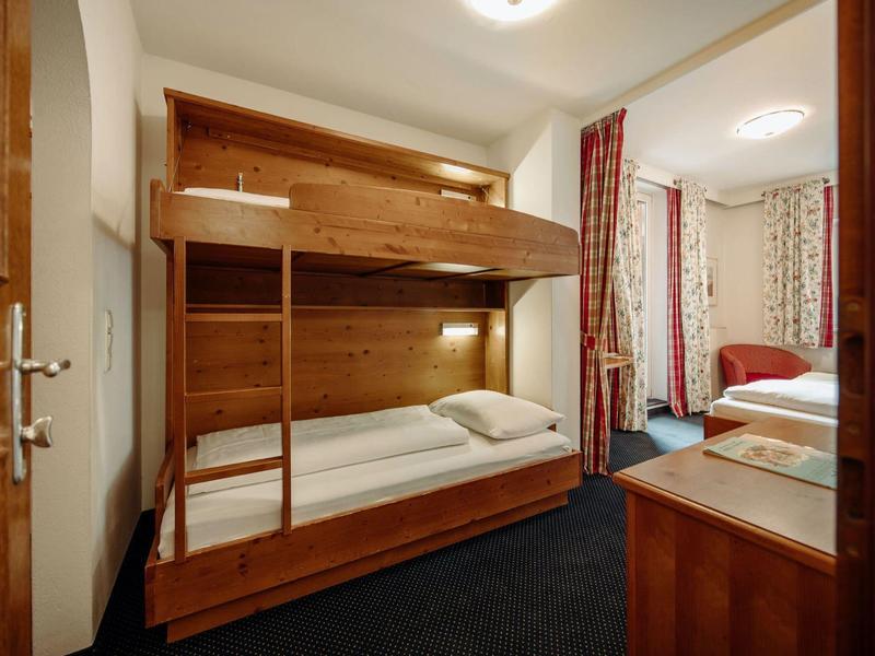 Schlafzimmer mit Etagenbett aus Holz, Teppichboden und einem Doppelbett im Hintergrund.