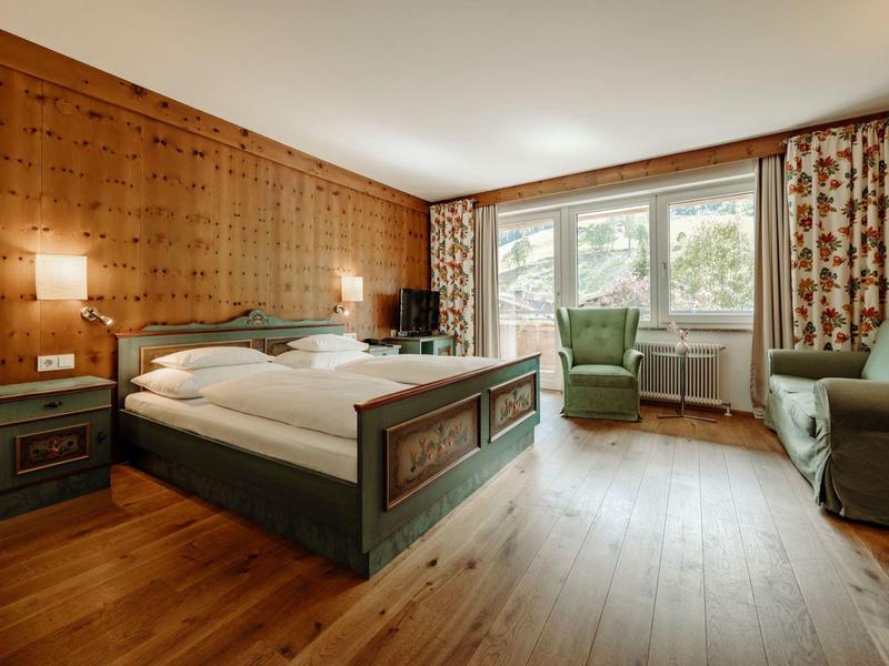 Gemütliches Schlafzimmer mit Holzwänden, einem großen Bett, Sessel und Sofa in warmem Licht.