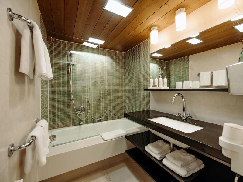 Modernes Bad mit Holzdecke, Wanne mit Glasduschwand, grüne Fliesen und großem Spiegel.