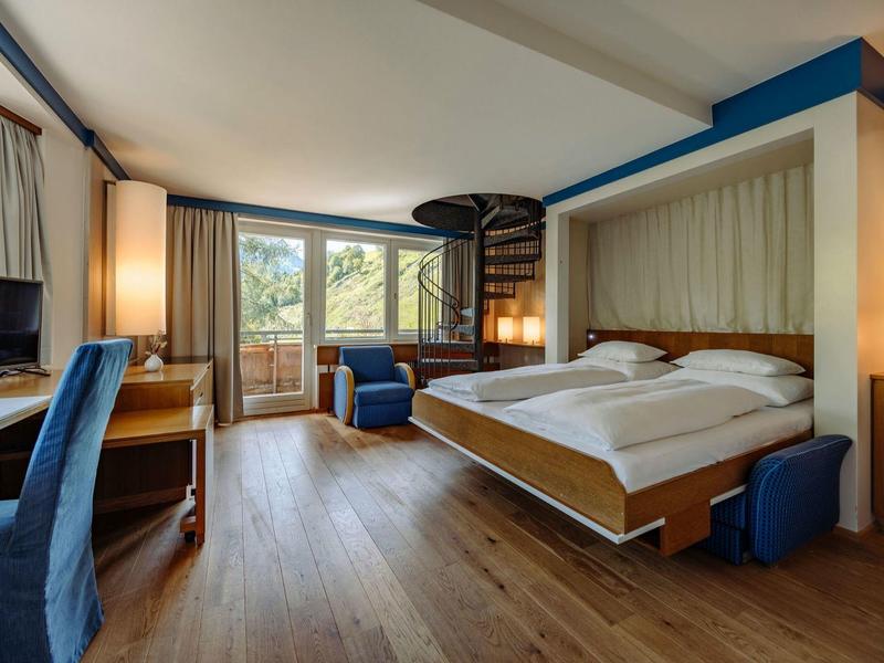 Modern eingerichtetes Hotelzimmer mit großem Bett, Holzfußboden und Sitzbereich am Fenster.