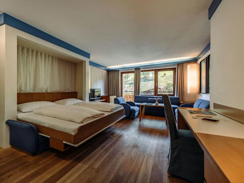 Modernes Hotelzimmer mit großem Bett, Holzboden und Sitzbereich mit Sofas und Schreibtisch