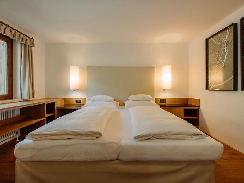 Schlichtes Hotelzimmer mit zwei Einzelbetten, Nachttischen und warmem Licht.