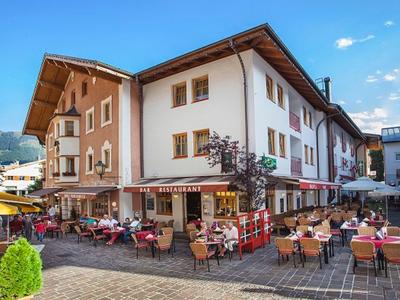 Straßencafé mit Tischen, Stühlen und Sonnenschirmen vor zweistöckigem Eckgebäude bei blauem Himmel.